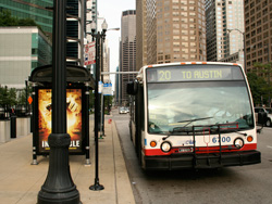 Bus #6700 at Madison and Jefferson working route #20 Madison on August 5, 2006. As part of the Bus Tracker pilot, the bus shelter at this location contains an LED sign which displays estimated arrival times along with the current time and temperature.